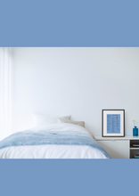 Bedroom with a bed, nightstand, and framed picture on a white wall.